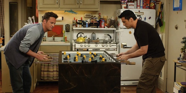 Chandler and Joey from Friends are playing foosball in an NYC apartment.