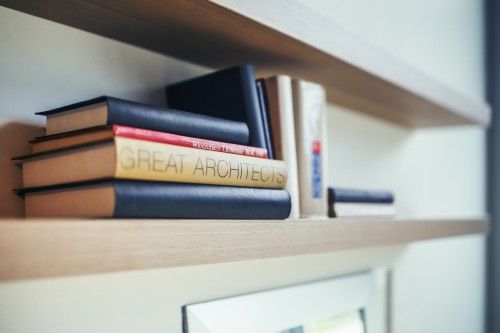 An organized wooden floating bookshelf is storing 11 different books.