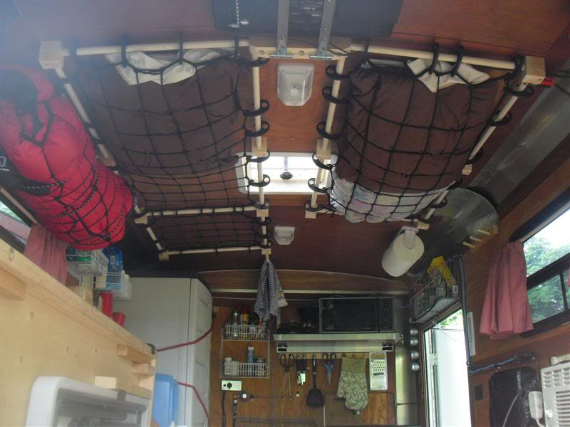 Two cargo nets are attached to a tiny trailer's ceiling and storing clothes.