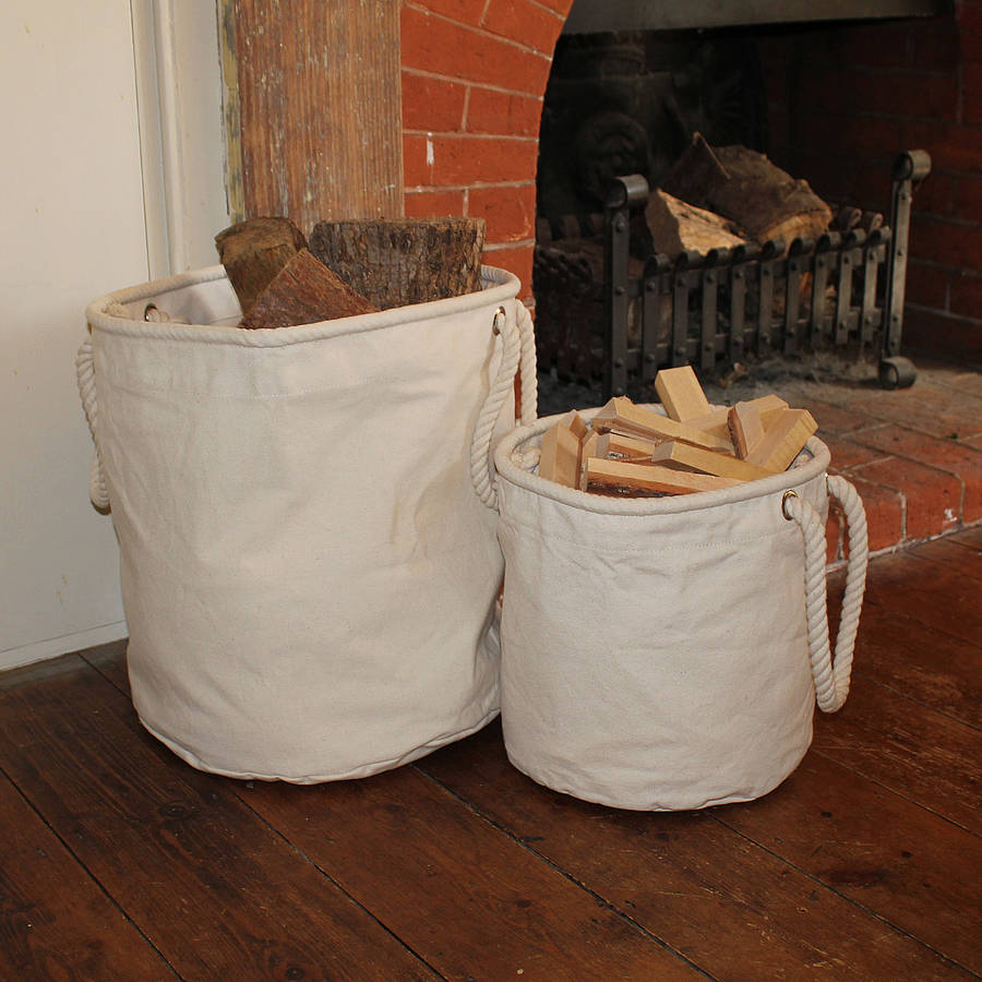A large and small canvas storage baskets are storing logs and kindling in a small apartment with a fireplace.