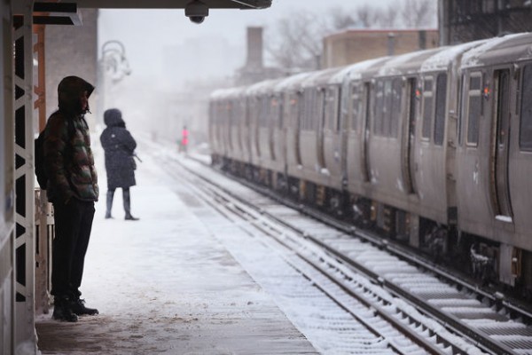 In an attempt to avoid cabin fever, two people are bundled up and waiting on a platform for the Chicago L while it's snowing outside.