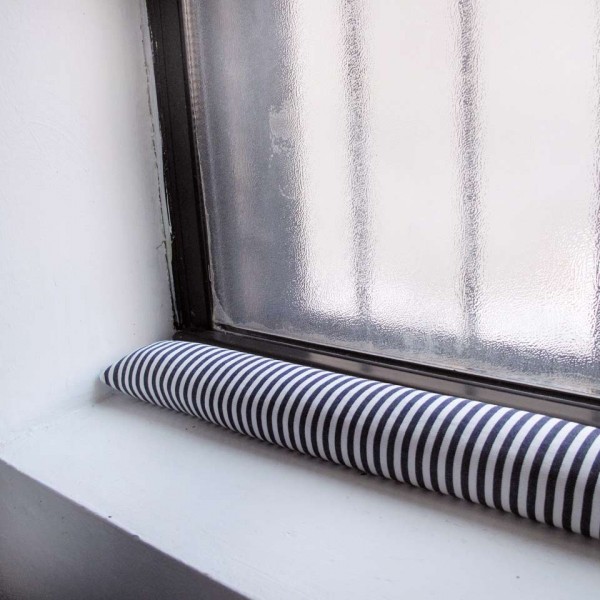 A DIY draft stopper with stripes is in front of an apartment window and blocking the cold, which helps you avoid cabin fever.