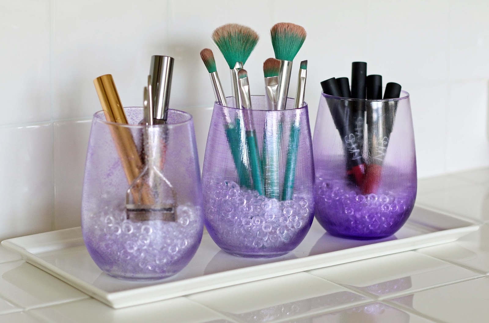 Three Purple Mod Podge glasses are used for makeup storage and organizing.