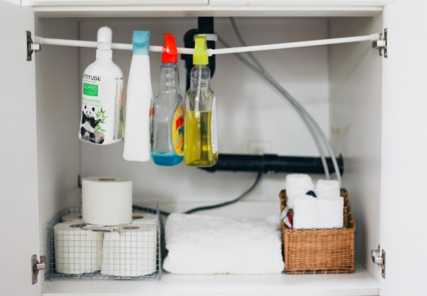 store bathroom cleaning supplies on a tension rod in a cabinet