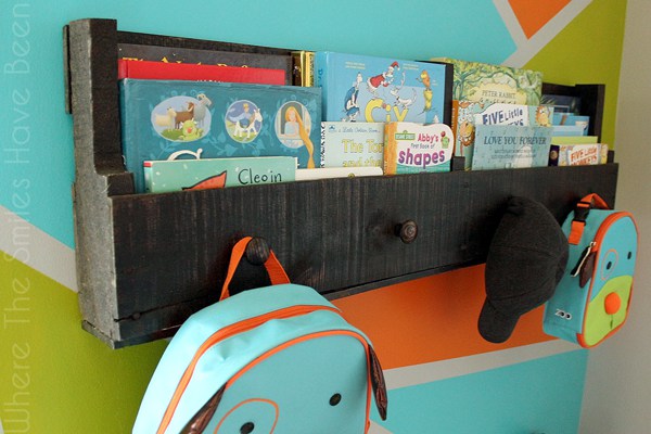 A reclaimed wood pallet bookshelf stores assorted children's books, backpacks, and a baseball hat.