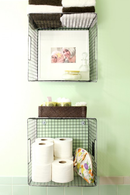 bathroom wall-mounted wire baskets storing toilet paper, toiletries, and towels