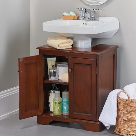wooden weatherby bathroom pedestal sink storing bathroom cleaning supplies, toilet paper, and other toiletries