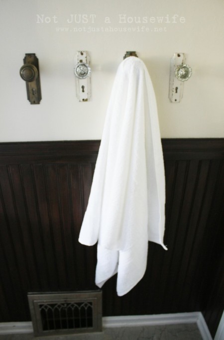 four wall-mounted door knobs, one of which is hanging a white towel