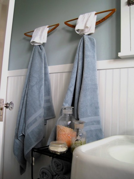 a creative bathroom storage hack is wall-mounted upside down hangers storing two body towels and two face towels