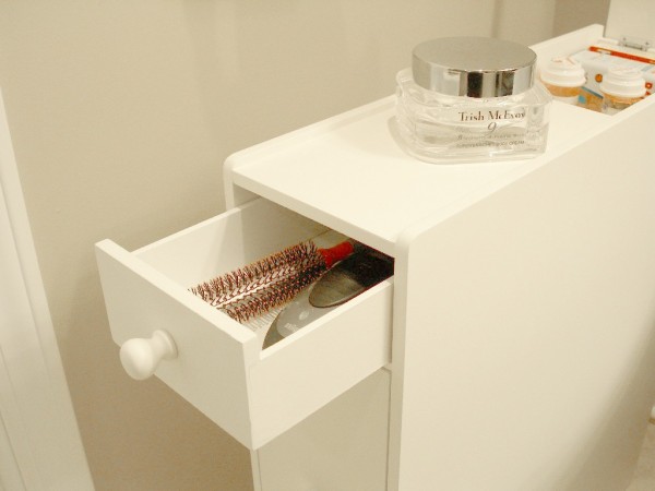 a white proman free-standing cabinet is storing a hair brush and a braun electric razor