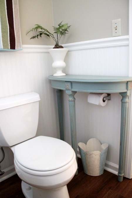 a small end table placed above a toilet paper roll is a cool bathroom storage hack