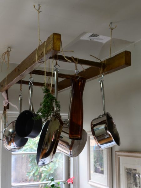 a wooden antique ladder/pot rack hanging from a ceiling is a brilliant kitchen storage solution for small apartments