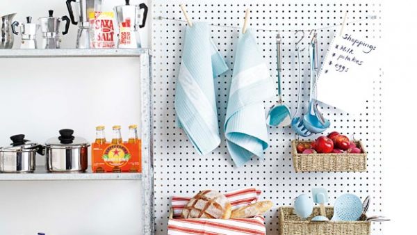 a kitchen wall-mounted diy pegboard is storing towels, cooking utensils, apples, bread, and a grocery list