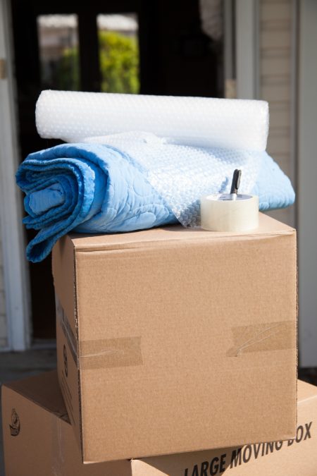 stacked moving boxes with packing tape, a moving blanket, and bubble wrap on top of the highest box