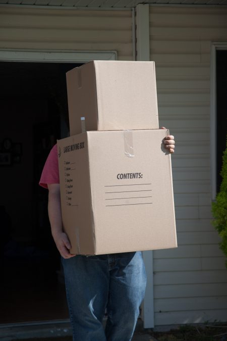 a man wearing blue jeans and a red shirt is carrying moving boxes out the door of a home