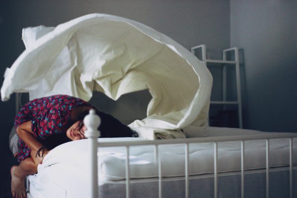 a young woman taking a break from making the bed by resting in fetal position