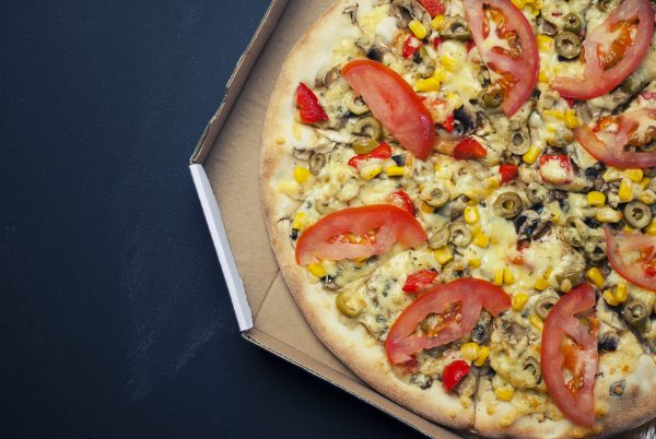 an open pizza box revealing a tomato, corn, olive, red pepper, and cheese pizza