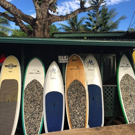 Rental SUP boards standing in the shade under a paddle board shop's roof