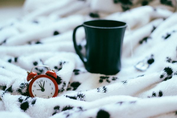 red alarm clock on a white and black paw print blanket and next to a tea mug