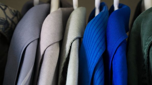 blue, green, and gray collared shirts hanging on white hangers in a closet