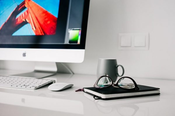 clean home office desk with a notebook, glasses, coffee mug, and imac on top