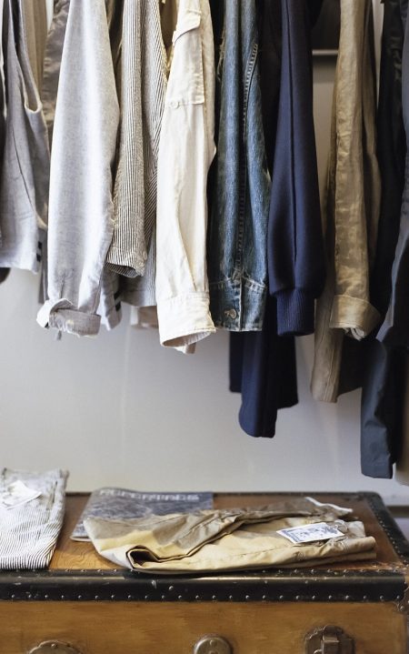 clothes hanging in a closet with a vintage trunk on the floor