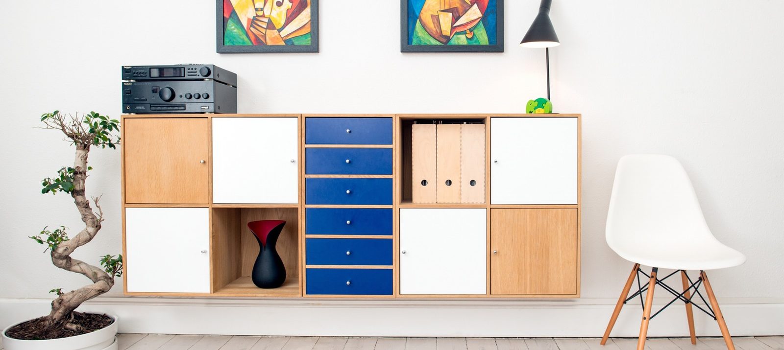 decluttered room with wall storage cubes, a plant, a white mid-century modern chair, and 2 paintings hanging on the wall