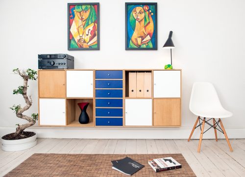 decluttered room with wall storage cubes, a plant, a white mid-century modern chair, and 2 paintings hanging on the wall