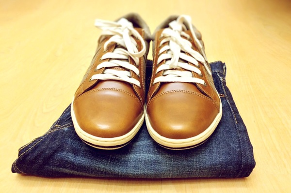 a pair of brown leather sneakers atop a pair of folded dark blue jeans