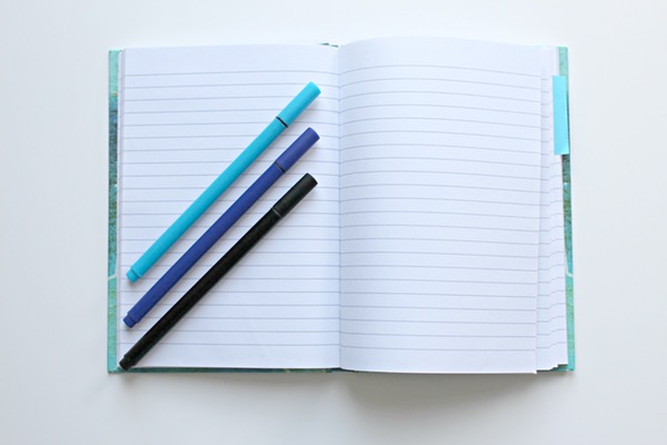 light blue, royal blue, and black pens atop an open light blue notebook