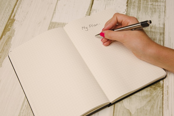 a woman's hand writing "my plan" in a notebook