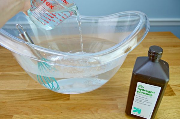 diy bleach and peroxide being mixed in a clear bowl with a whisk