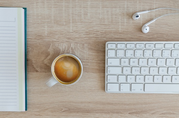 overhead view of a clean wooden workspace with a notebook, coffee mug, magic keyboard, and earpods