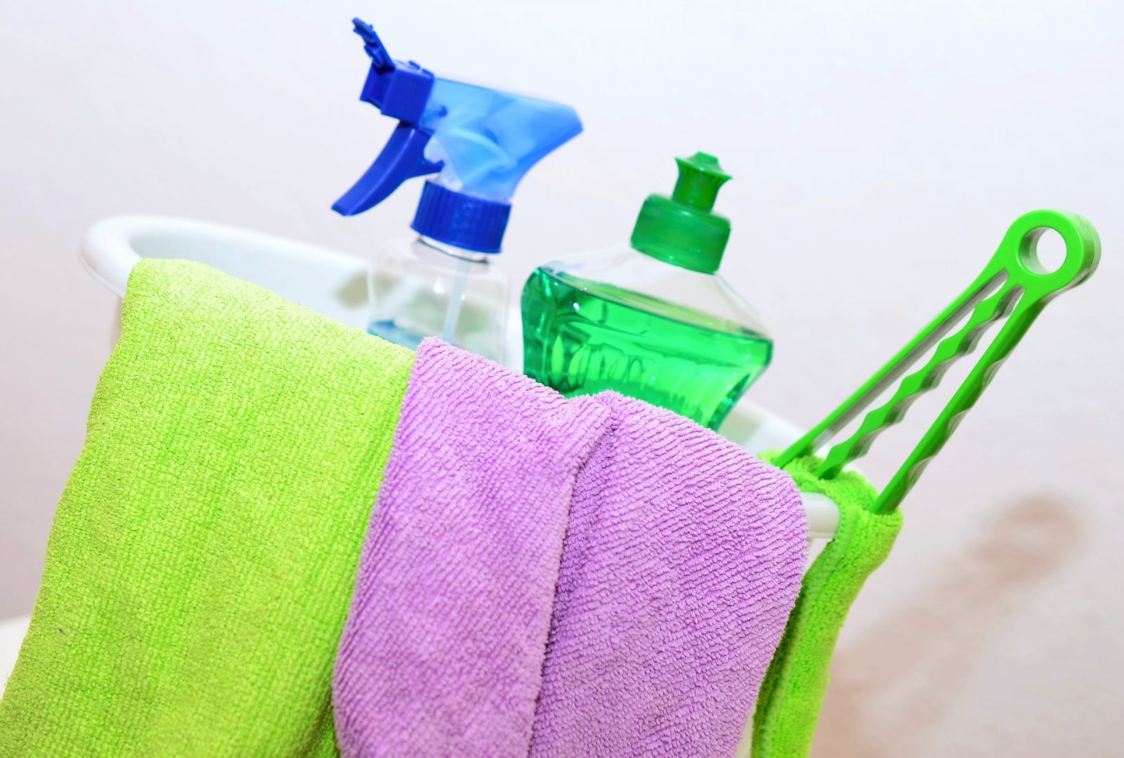 spring cleaning tips and tricks: a bucket with two towels, a cleaning spray bottle, green dish soap, and a scrubber with handle