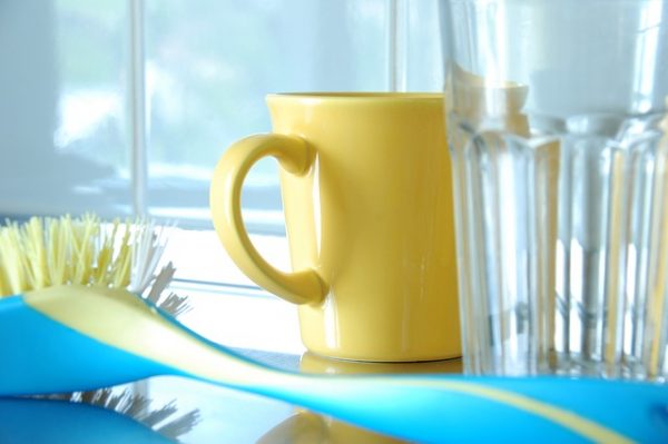 clean yellow coffee mug, drinking glass, and dish brush in a kitchen