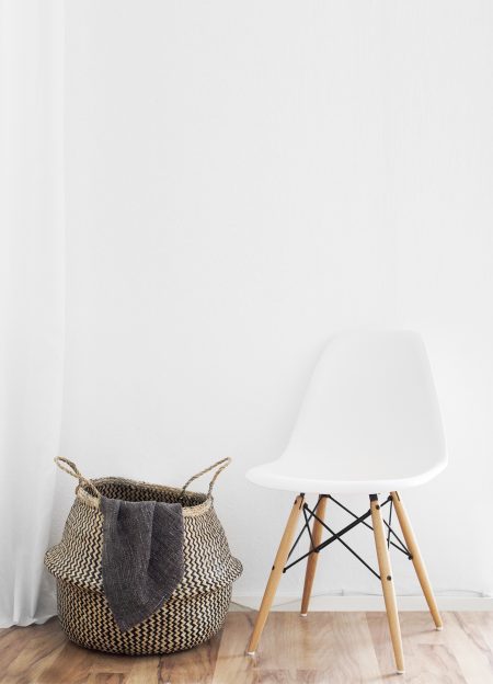 laundry basket next to a white eames style vortex chair on a wooden floor in a clean home