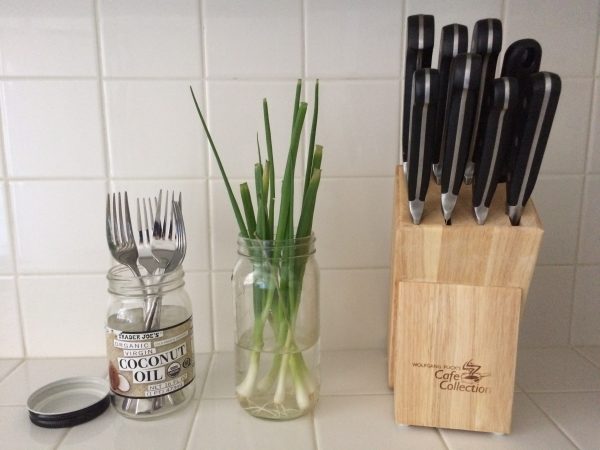 a mason jar storing forks, a mason jar storing scallions in water, and a wooden knife block by paige smith