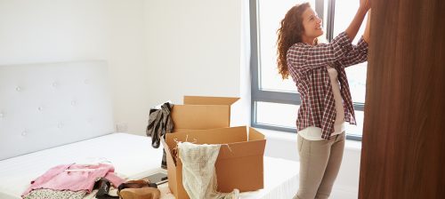 what to store and toss before moving into a new house: a woman packing clothes into boxes in a bedroom