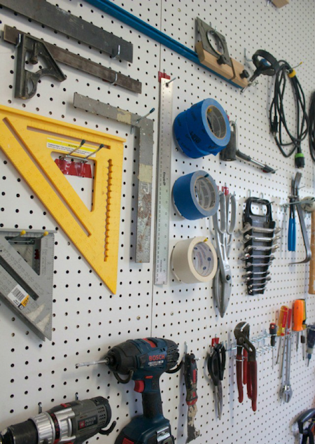 white diy pegboard with hooks storing tools in a garage