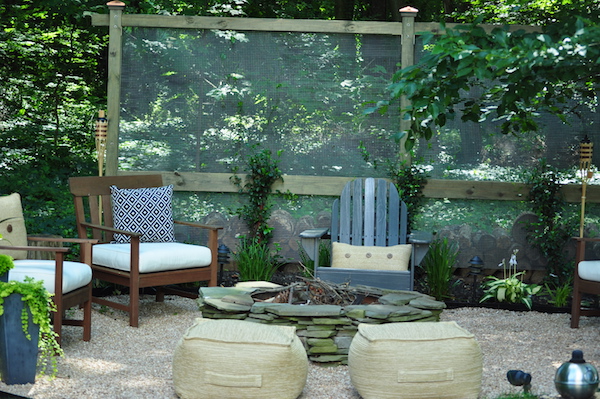 alison giese designed this backyard fire pit decor with a garden screen, outdoor chairs, cushions, pillows, plants, bamboo torches, and a small bbq grill