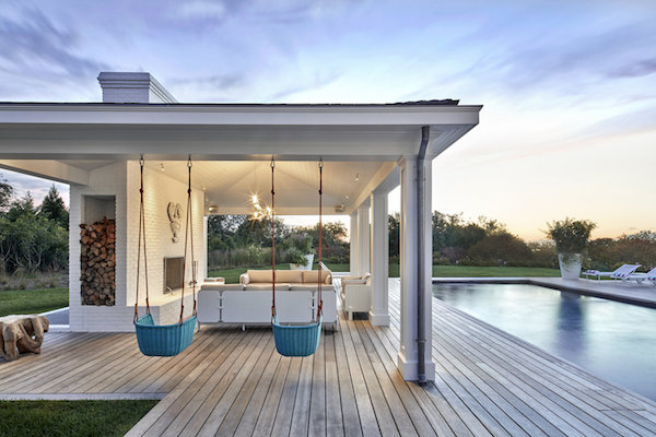 ghislaine vinas' poolside patio with a fireplace, 3 sofas, and 2 outdoor hanging chairs