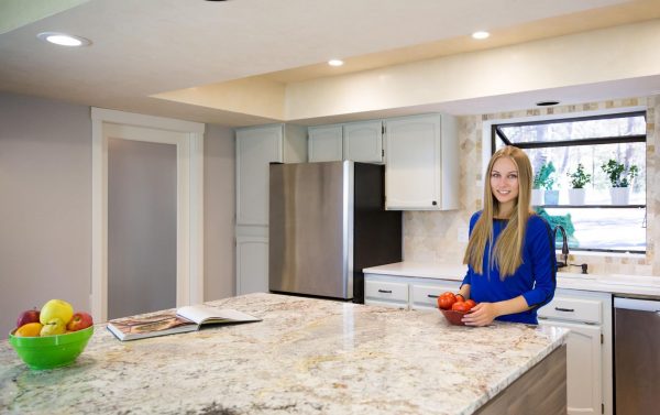 blonde woman holding a basket of tomatoes and standing behind a marble kitchen island