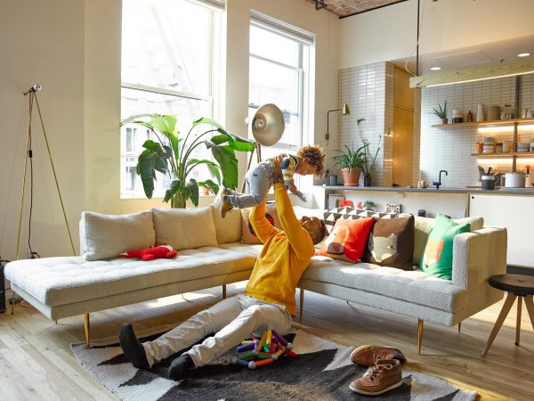 a father sitting on the floor of a stylish living room while lifting his son in the air