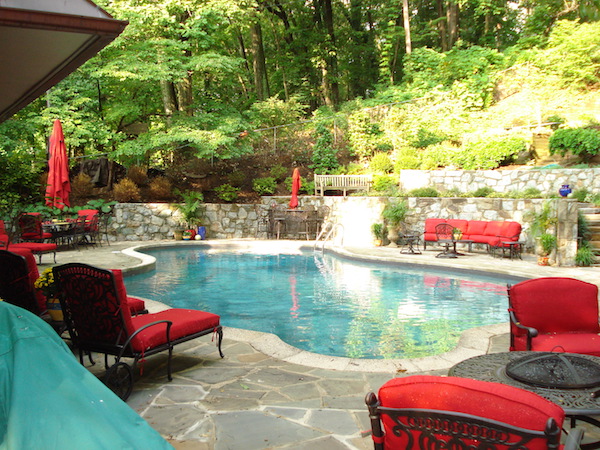 june shea backyard seating with red cushions, outdoor tables and umbrellas, and a pool