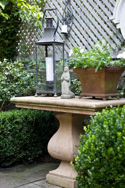 lantern, small stone statue, and a planter on top of a stone table in a backyard designed by kelley proxmire