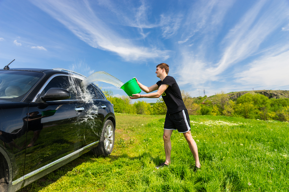 car garage spring cleaning checklist: guy washing his car in the grass