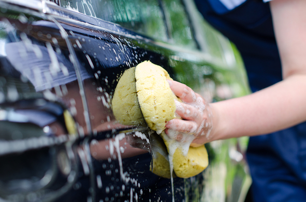 A woman wipes the outside of her car with a sponge.