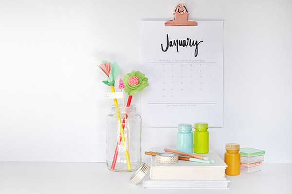 a hand-lettered calendar hanging above a desk with flowers on it 
