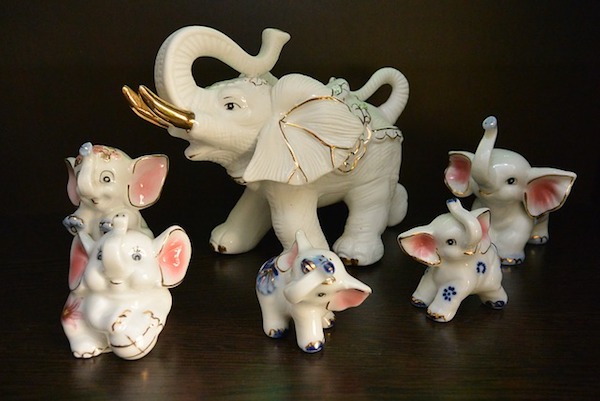 Porcelain elephants are lined up on a dark surface