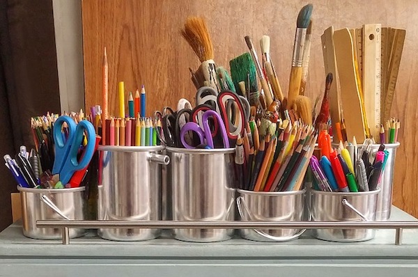 Colorful art supplies are grouped together in six tin canisters